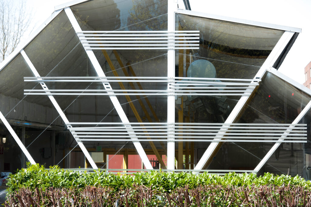 Front view of the Urban Commons Lab building. The building has 6 beams emanating from the ground outward, three levels of vertical beams, and a multi level roof.