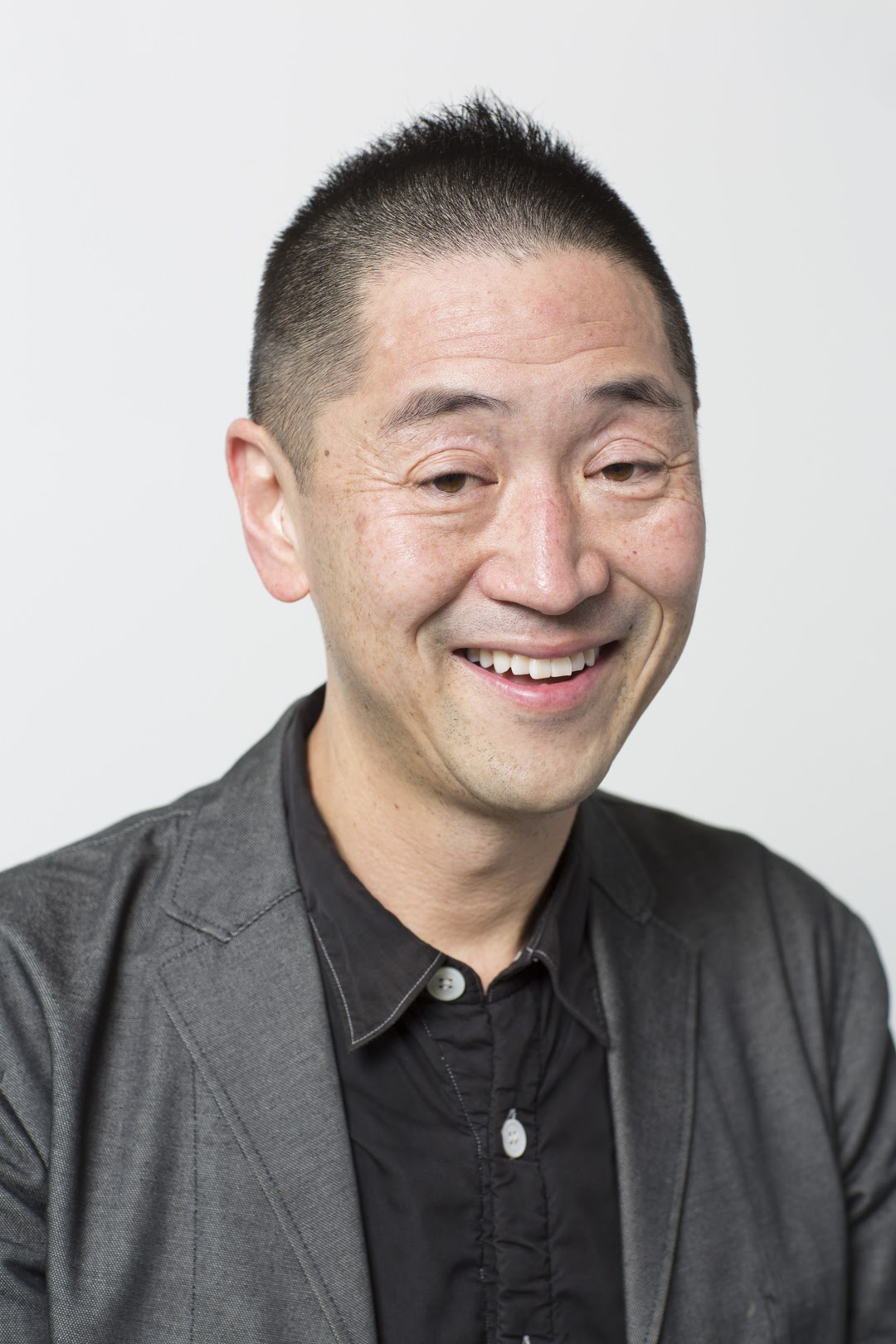 Headshot of Ken Tadashi Oshima, he's wearing a black shirt and grey jacket