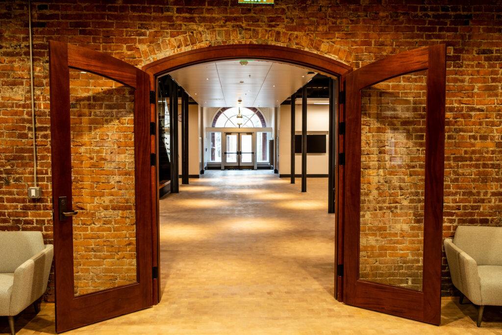 Interior of a brick building with two doors swung open and a white chair on either side of the doorway entrance