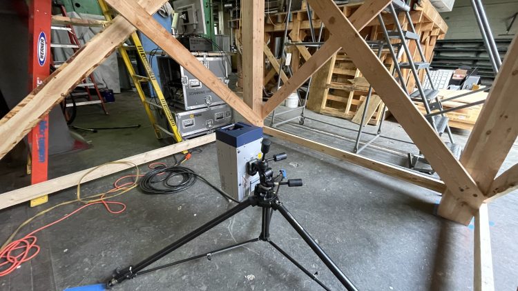 The vibrometer, on loan from Andy Piacsek, Central Washington University Associate Professor of Physics and acoustics specialist, sits beneath the mass-timber floor. It shoots a laser beam towards reflective stickers on the floor to measure vibrations as a proxy for sound.